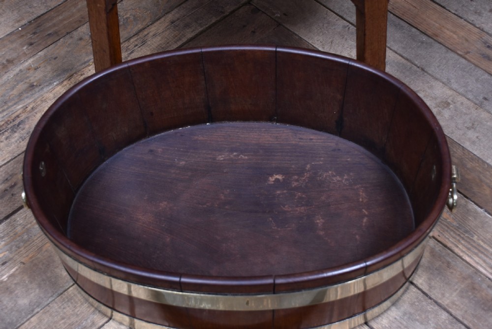 An oval George III mahogany wine cooler bound with two wide brass bands, featuring brass side handles and supported on a fitted wooden stand with four tapered legs. View V