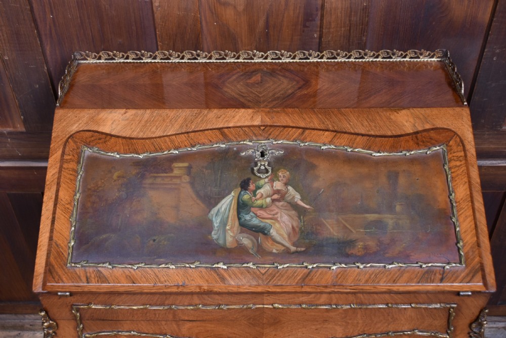 A 19th-century French rosewood bureau de dame featuring slender cabriole legs, brass mounts, a brass gallery top, and a hand-painted scene on the slanted flap front. View V