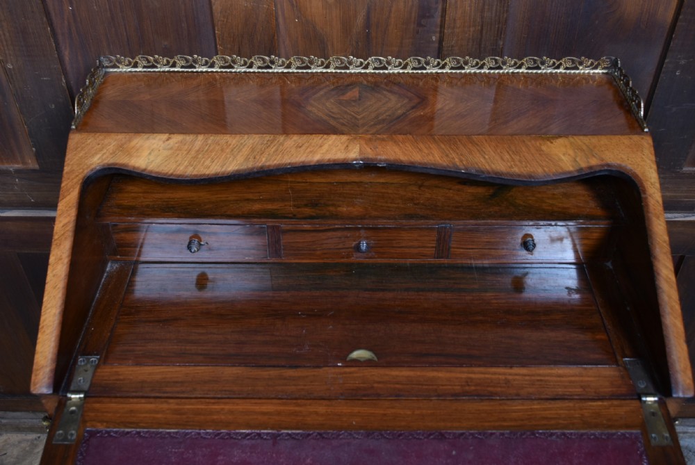 A 19th-century French rosewood bureau de dame featuring slender cabriole legs, brass mounts, a brass gallery top, and a hand-painted scene on the slanted flap front. View XI