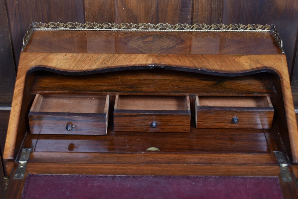 A 19th-century French rosewood bureau de dame featuring slender cabriole legs, brass mounts, a brass gallery top, and a hand-painted scene on the slanted flap front. View XII