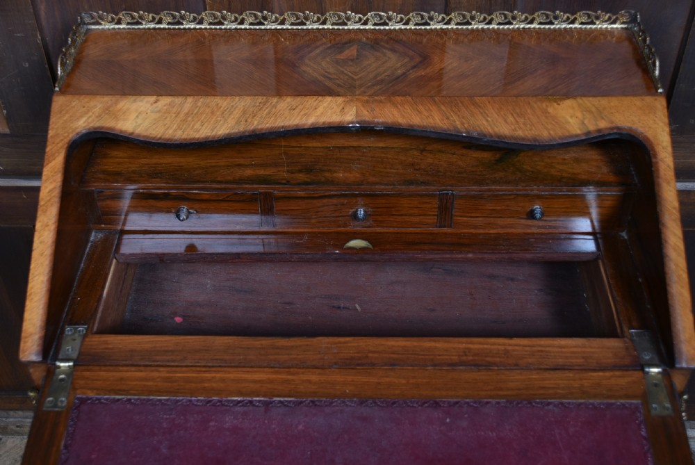 A 19th-century French rosewood bureau de dame featuring slender cabriole legs, brass mounts, a brass gallery top, and a hand-painted scene on the slanted flap front. View XIII