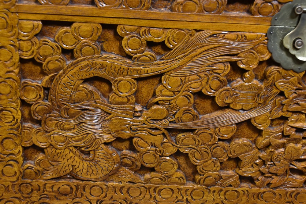 A deeply carved warm brown camphor wood storage chest featuring relief carvings of dragons and birds with a central brass clasp. View II