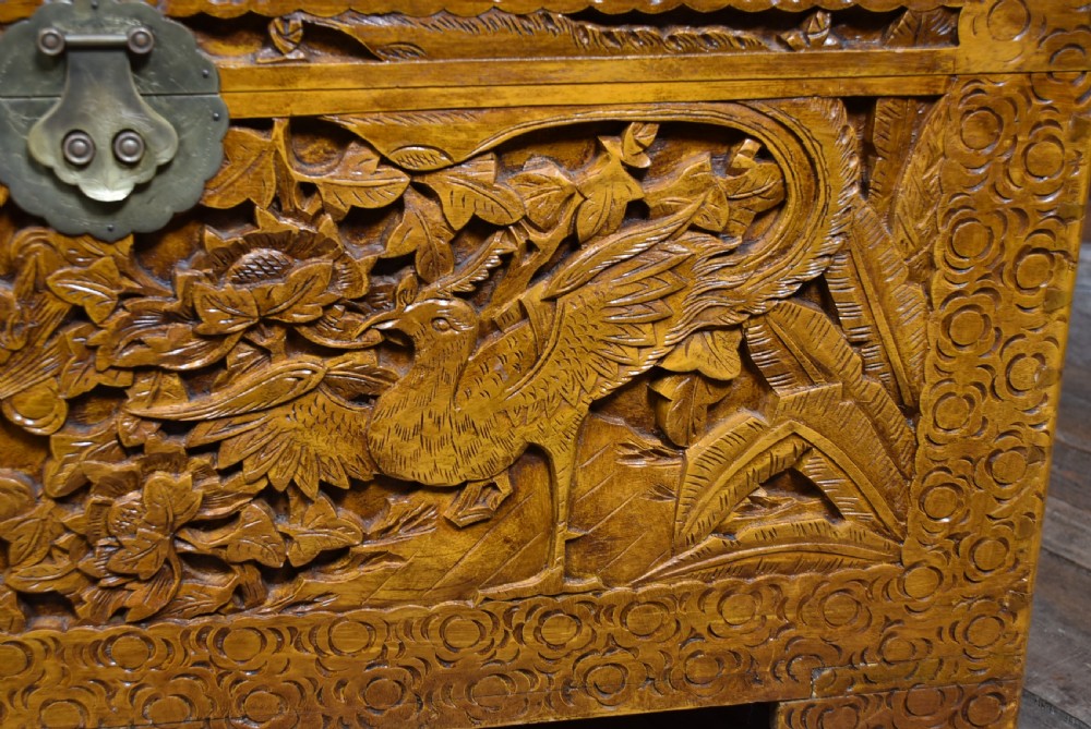 A deeply carved warm brown camphor wood storage chest featuring relief carvings of dragons and birds with a central brass clasp. View III