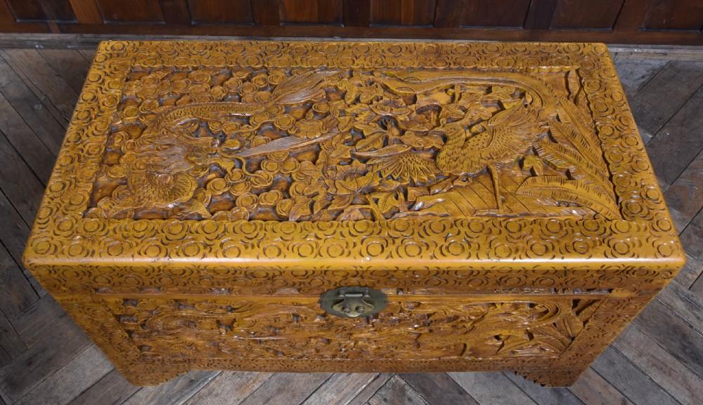A deeply carved warm brown camphor wood storage chest featuring relief carvings of dragons and birds with a central brass clasp. View V