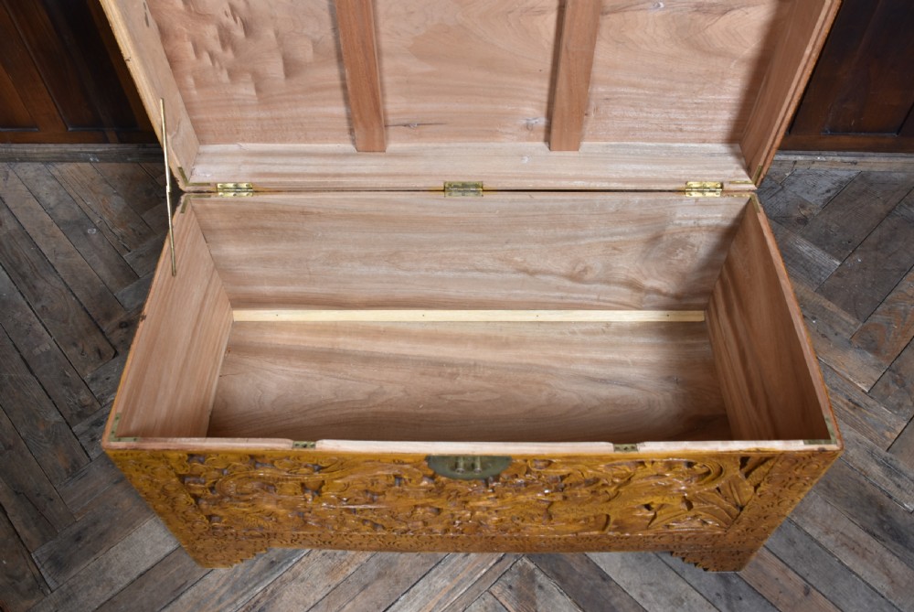 A deeply carved warm brown camphor wood storage chest featuring relief carvings of dragons and birds with a central brass clasp. View X
