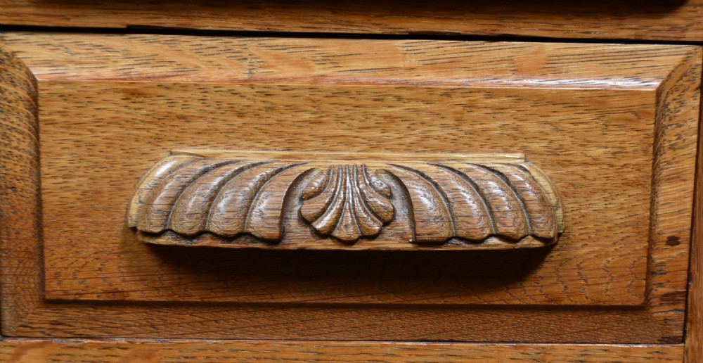 A traditional oak roll-top desk featuring a slatted wooden tambour cover, central kneehole, and twin pedestals fitted with carved handles. View V