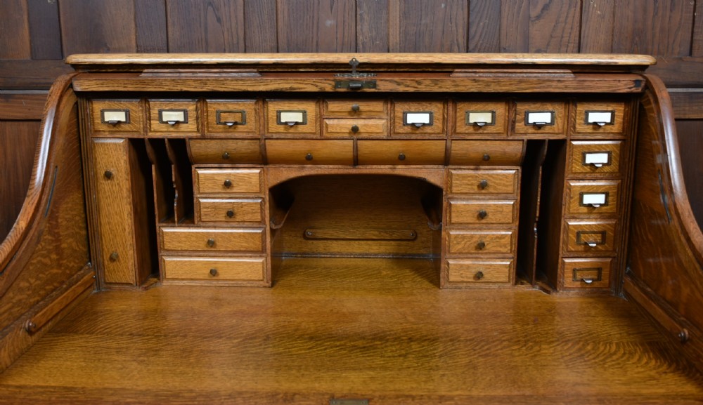 A traditional oak roll-top desk featuring a slatted wooden tambour cover, central kneehole, and twin pedestals fitted with carved handles. View VI