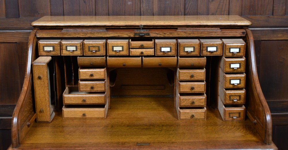 A traditional oak roll-top desk featuring a slatted wooden tambour cover, central kneehole, and twin pedestals fitted with carved handles. View VIII