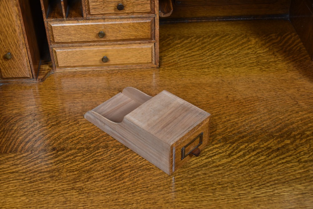 A traditional oak roll-top desk featuring a slatted wooden tambour cover, central kneehole, and twin pedestals fitted with carved handles. View IX