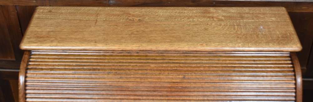 A traditional oak roll-top desk featuring a slatted wooden tambour cover, central kneehole, and twin pedestals fitted with carved handles. View XVIII