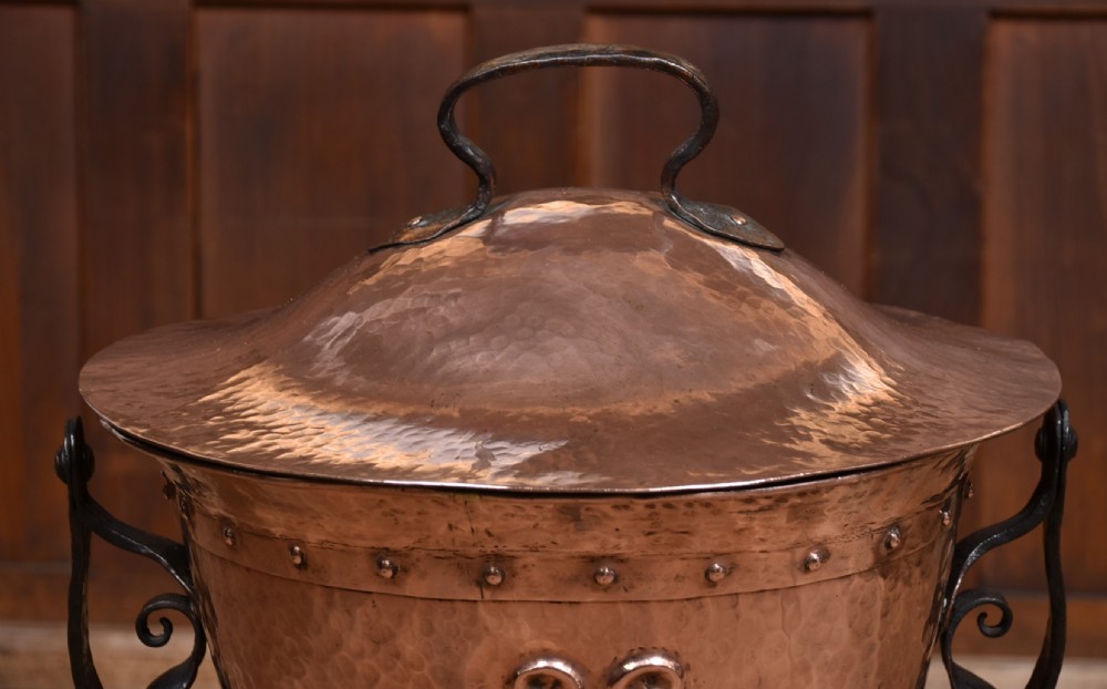 A hammered copper bucket featuring a domed lid and embossed Art Nouveau motif, set within a black wrought iron tripod frame. View III