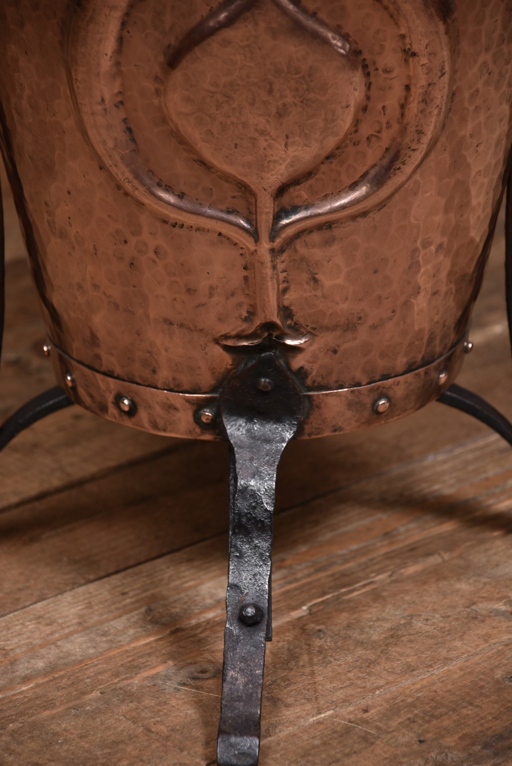 A hammered copper bucket featuring a domed lid and embossed Art Nouveau motif, set within a black wrought iron tripod frame. View VIII