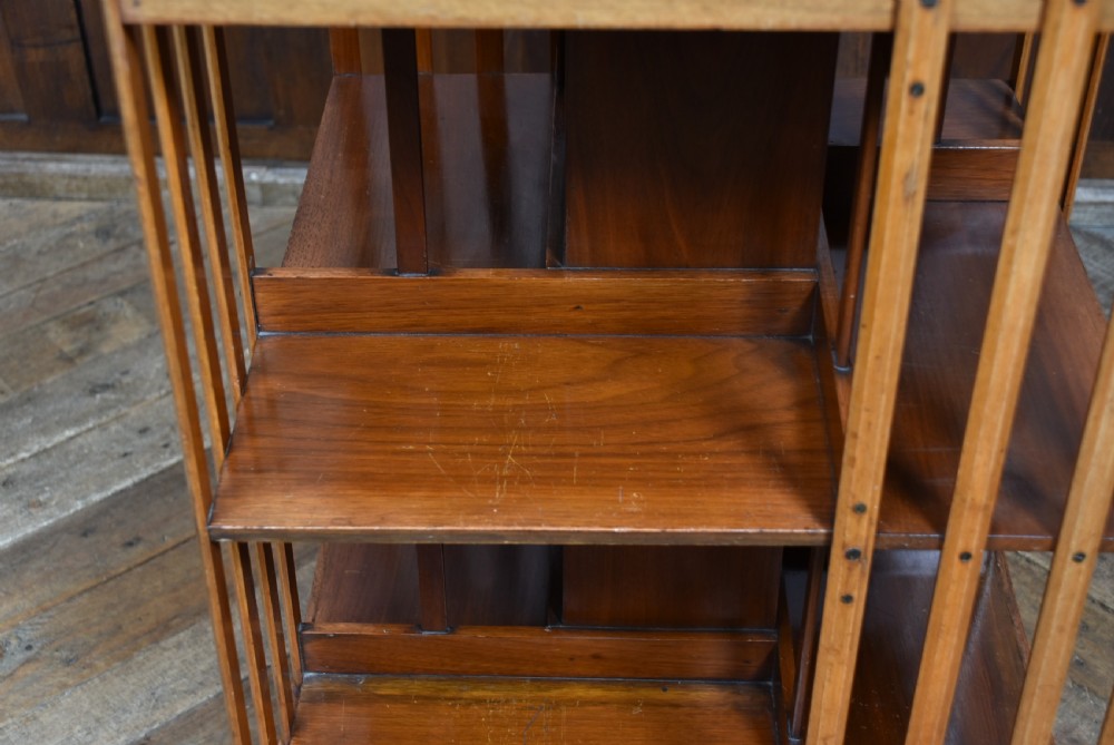 An Edwardian square walnut revolving bookcase featuring two tiers with vertical slatted sides and a flat moulded top surface. View VII