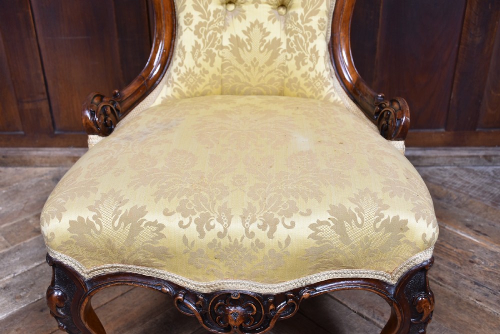 A Victorian carved walnut spoon-back nursing chair with button-tufted gold damask upholstery, cabriole front legs, and ceramic casters. View XI