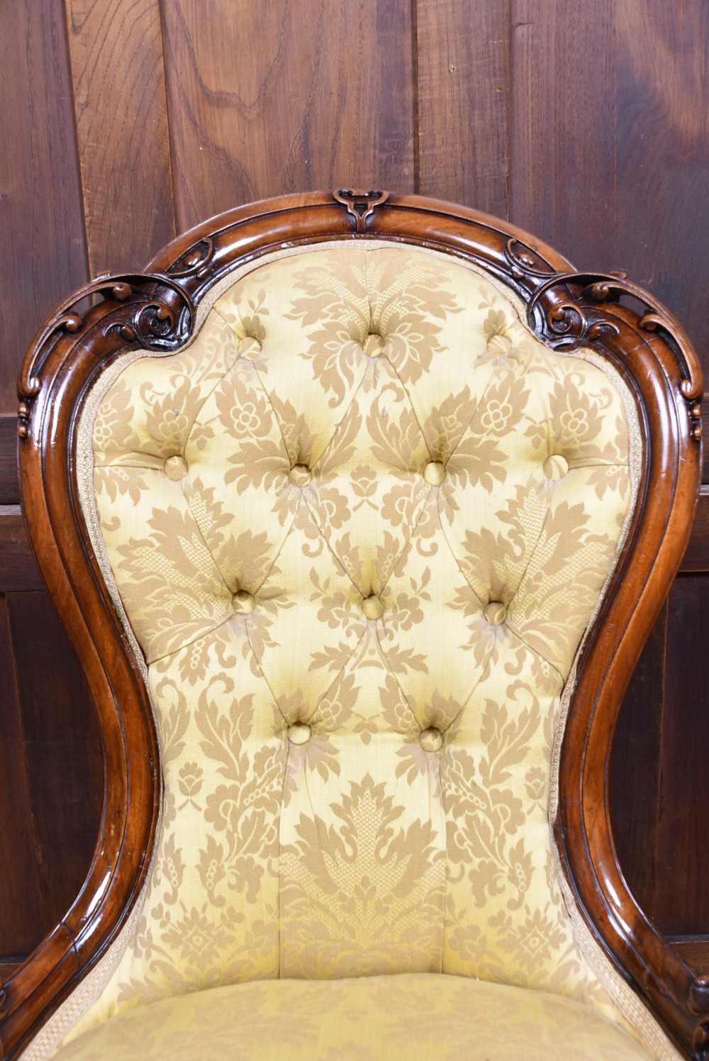 A Victorian carved walnut spoon-back nursing chair with button-tufted gold damask upholstery, cabriole front legs, and ceramic casters. View XII