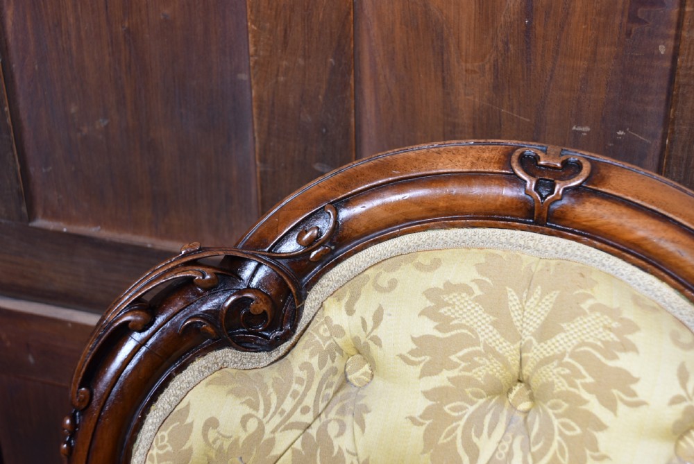 A Victorian carved walnut spoon-back nursing chair with button-tufted gold damask upholstery, cabriole front legs, and ceramic casters. View XIII