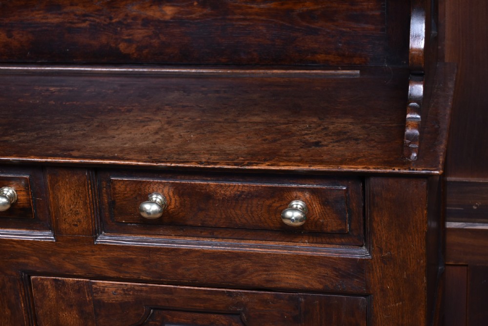 A 19th-century dark oak French provincial dresser featuring an open upper plate rack with a scalloped top apron over three drawers and two panelled cupboard doors. View III