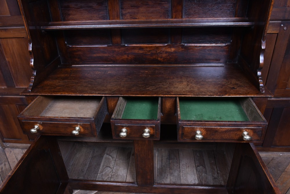 A 19th-century dark oak French provincial dresser featuring an open upper plate rack with a scalloped top apron over three drawers and two panelled cupboard doors. View VII