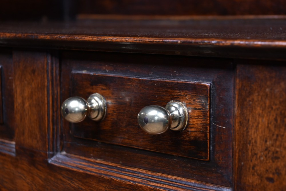 A 19th-century dark oak French provincial dresser featuring an open upper plate rack with a scalloped top apron over three drawers and two panelled cupboard doors. View IX