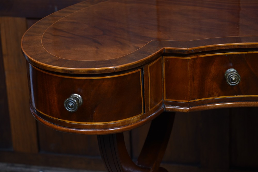 An Edwardian mahogany kidney-shaped desk featuring satinwood inlay, three frieze drawers with round brass handles, swept legs, and brass castors. View VI
