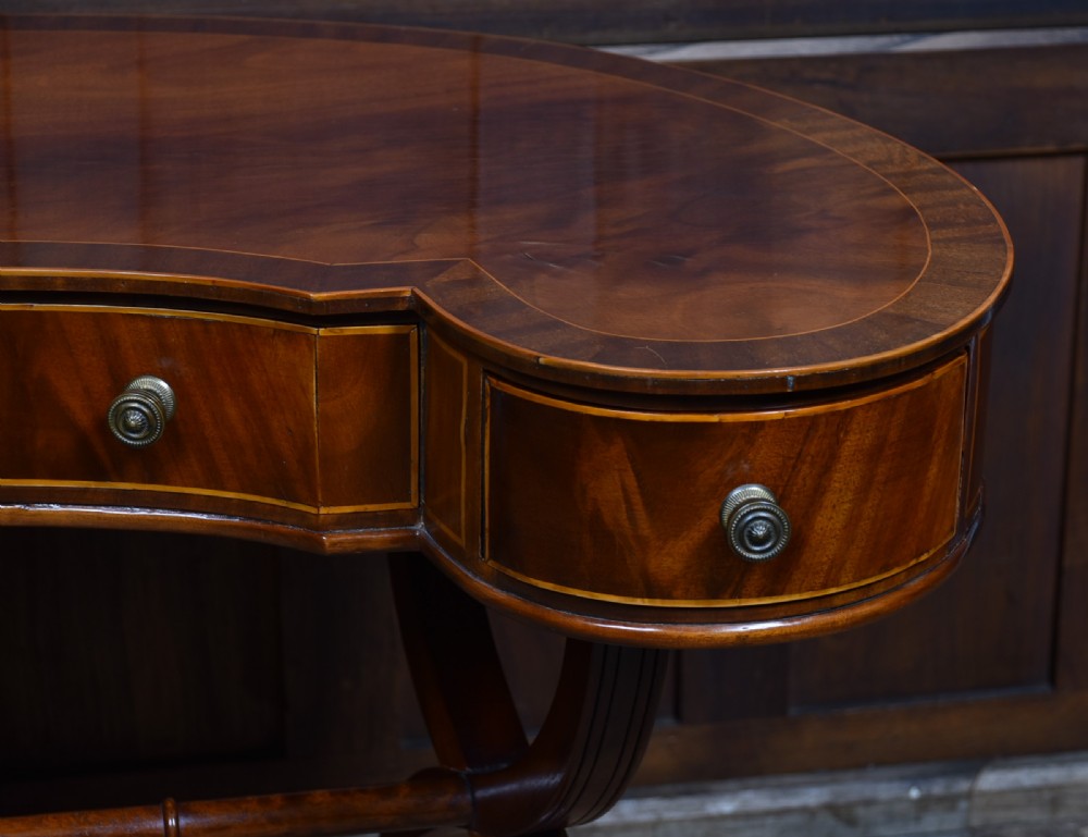 An Edwardian mahogany kidney-shaped desk featuring satinwood inlay, three frieze drawers with round brass handles, swept legs, and brass castors. View VII