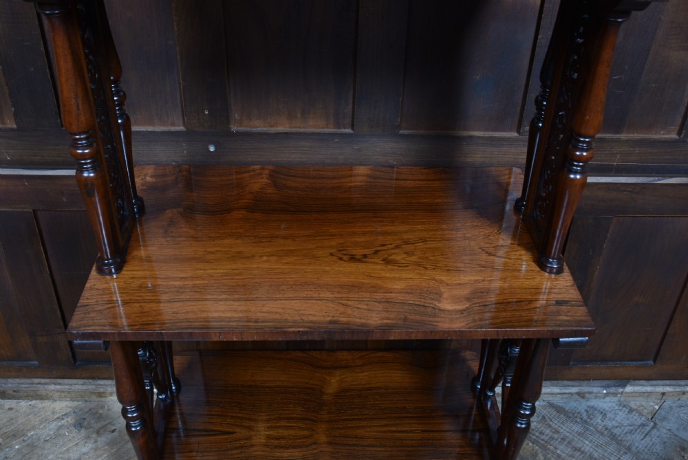 A three-tiered Victorian rosewood whatnot shelf featuring turned support columns, carved top details, and a single lower drawer with twin circular knobs. View V