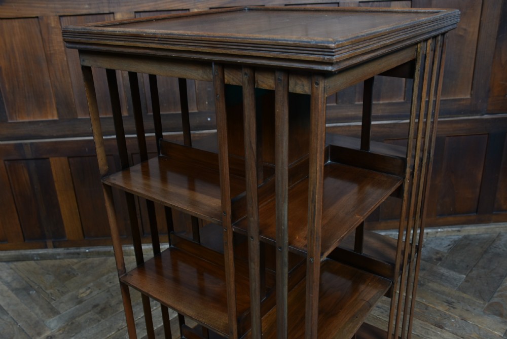 An Edwardian warm brown walnut three-tier revolving bookcase with vertical slatted sides resting on castors. View V