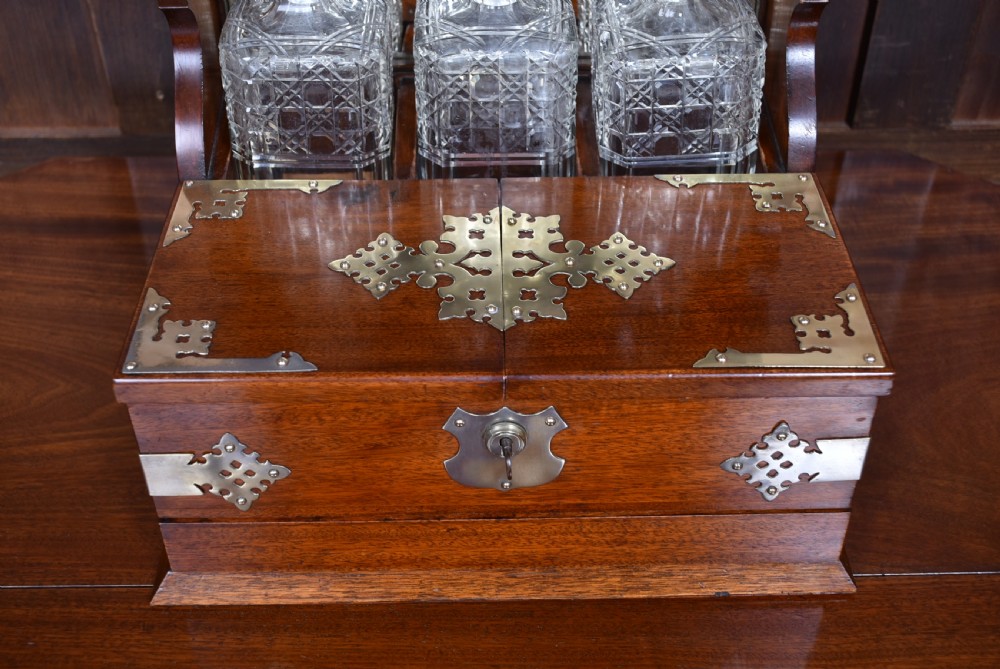 An Edwardian polished mahogany tantalus and games compendium featuring three cut crystal decanters and silver-toned brass strapwork mounts. View VI