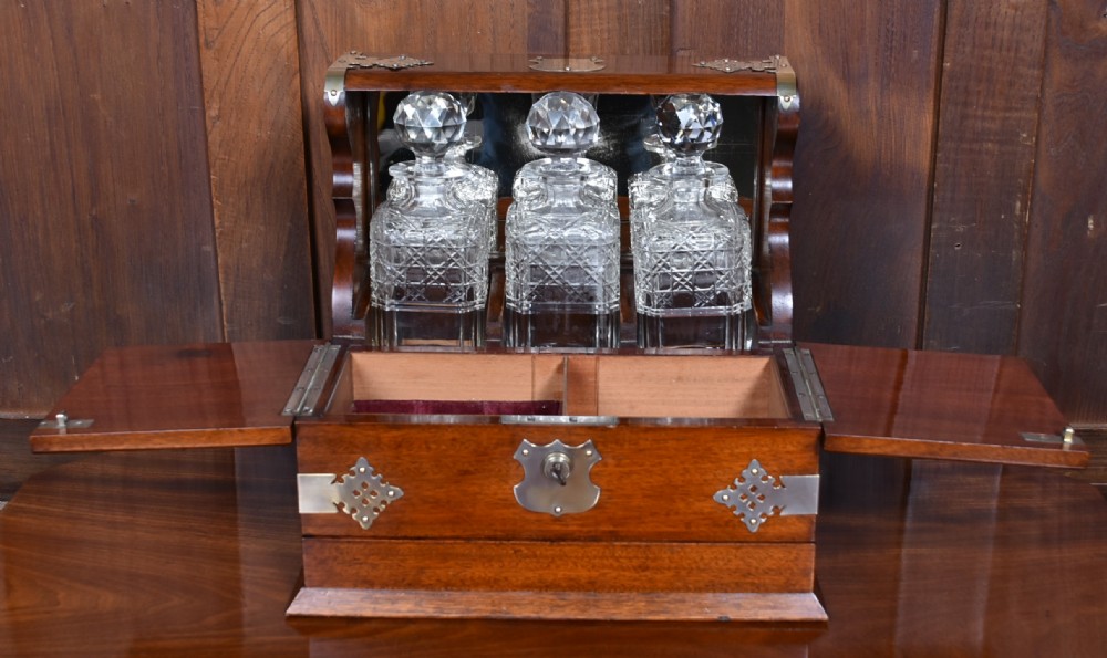 An Edwardian polished mahogany tantalus and games compendium featuring three cut crystal decanters and silver-toned brass strapwork mounts. View VIII