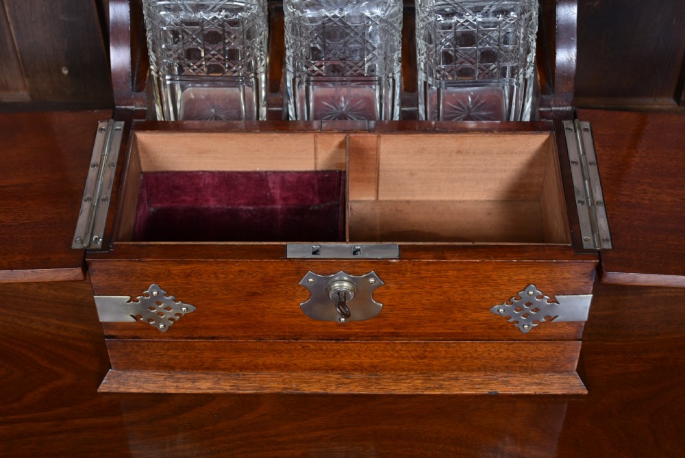 An Edwardian polished mahogany tantalus and games compendium featuring three cut crystal decanters and silver-toned brass strapwork mounts. View IX