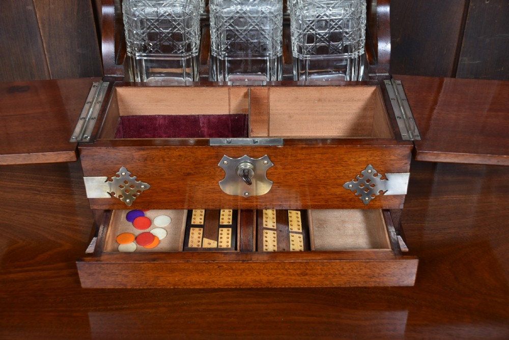 An Edwardian polished mahogany tantalus and games compendium featuring three cut crystal decanters and silver-toned brass strapwork mounts. View XI