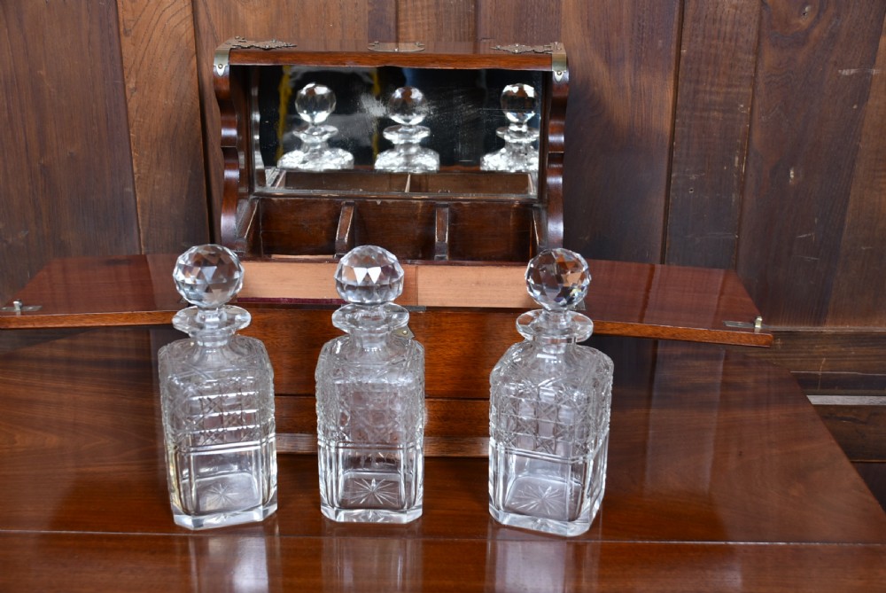 An Edwardian polished mahogany tantalus and games compendium featuring three cut crystal decanters and silver-toned brass strapwork mounts. View XIII