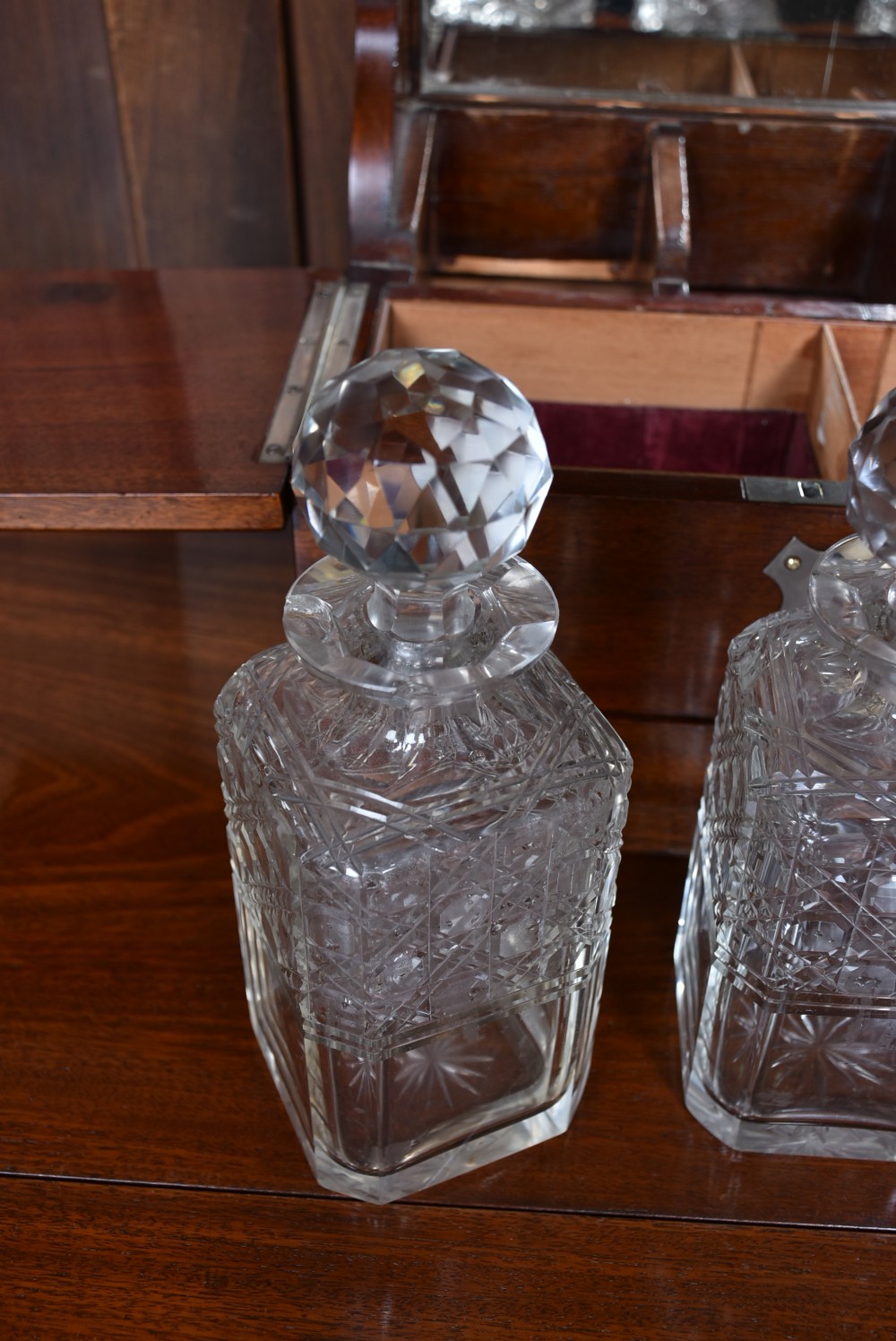 An Edwardian polished mahogany tantalus and games compendium featuring three cut crystal decanters and silver-toned brass strapwork mounts. View XIV