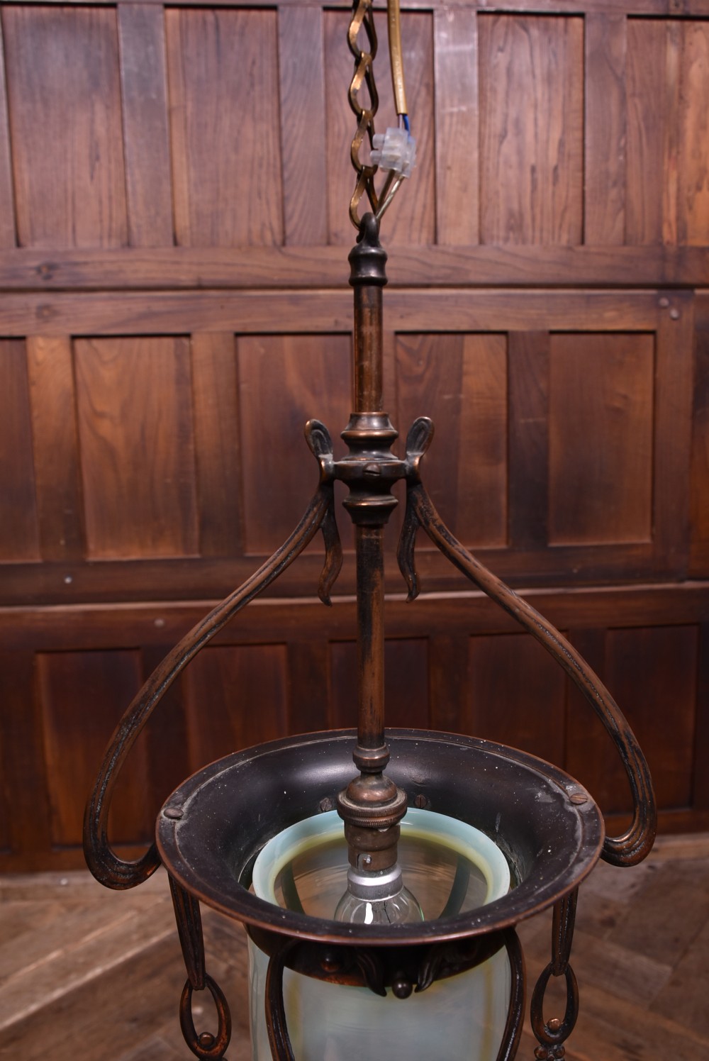 An Art Nouveau copper pendant light fitting featuring a whiplash scroll frame enclosing a pale opalescent glass shade suspended from a chain. View VII