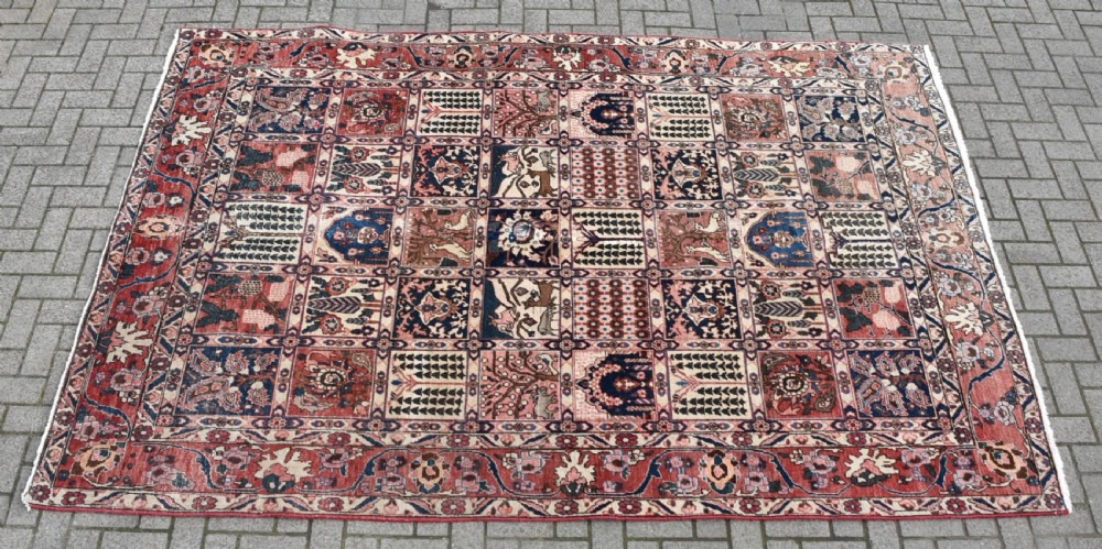 A hand-knotted Persian wool rug featuring a grid panel design with tree and floral motifs enclosed by a detailed terracotta border.