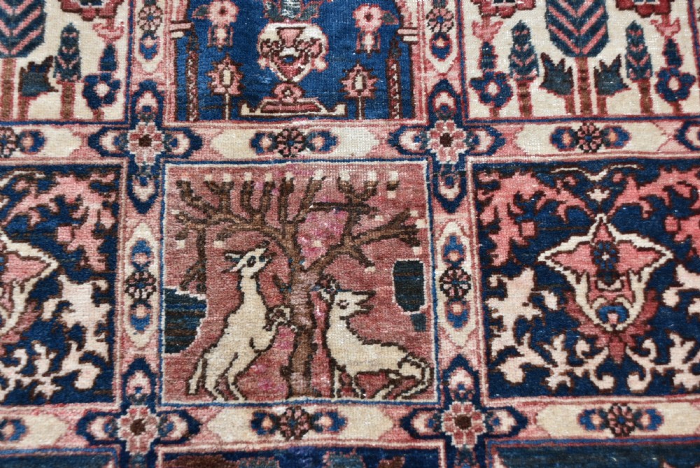 A hand-knotted Persian wool rug featuring a grid panel design with tree and floral motifs enclosed by a detailed terracotta border. View X