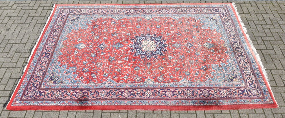 A large hand-knotted vintage Persian rug featuring a central dark blue medallion surrounded by a detailed red field filled with floral arabesque patterns and framed by intricate borders.