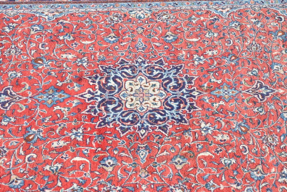 A large hand-knotted vintage Persian rug featuring a central dark blue medallion surrounded by a detailed red field filled with floral arabesque patterns and framed by intricate borders. View II