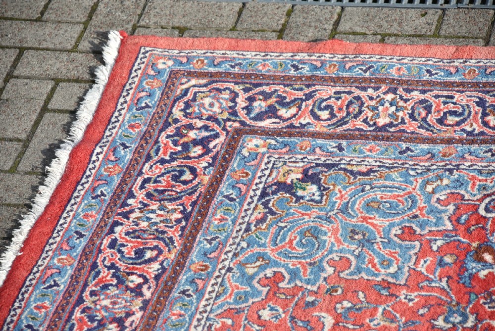 A large hand-knotted vintage Persian rug featuring a central dark blue medallion surrounded by a detailed red field filled with floral arabesque patterns and framed by intricate borders. View IV