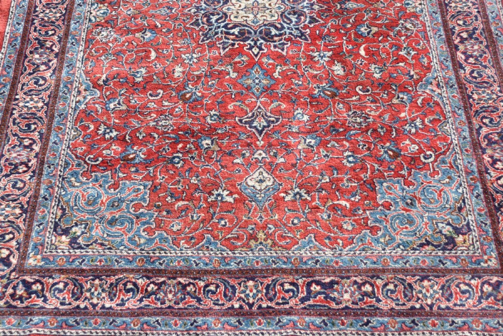 A large hand-knotted vintage Persian rug featuring a central dark blue medallion surrounded by a detailed red field filled with floral arabesque patterns and framed by intricate borders. View VII