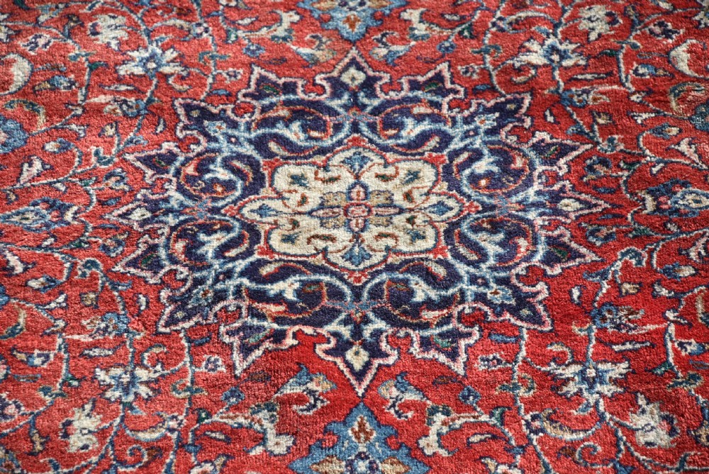 A large hand-knotted vintage Persian rug featuring a central dark blue medallion surrounded by a detailed red field filled with floral arabesque patterns and framed by intricate borders. View VIII