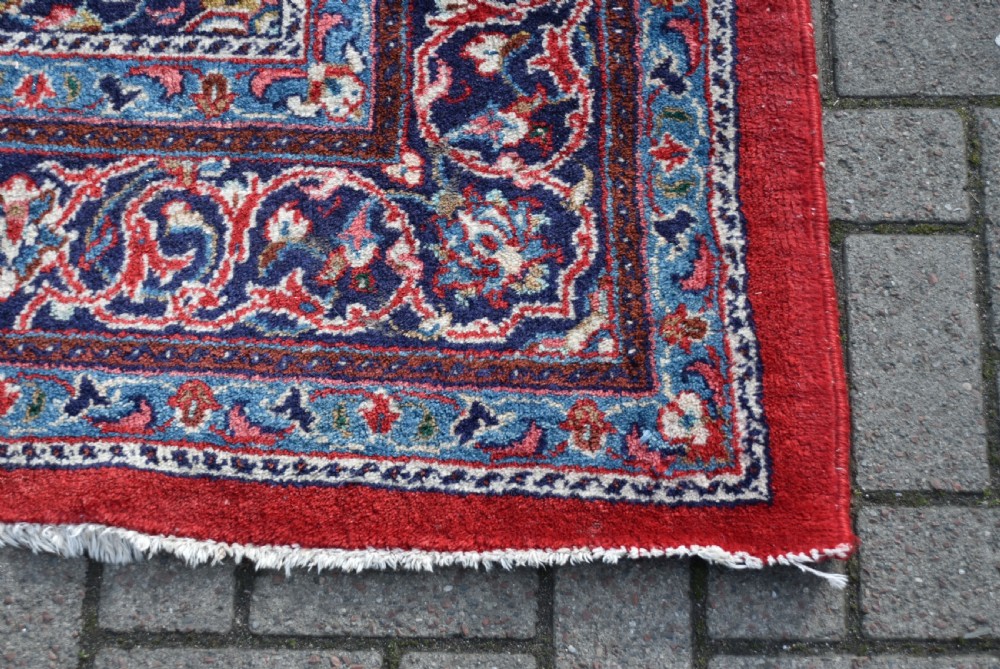 A large hand-knotted vintage Persian rug featuring a central dark blue medallion surrounded by a detailed red field filled with floral arabesque patterns and framed by intricate borders. View IX