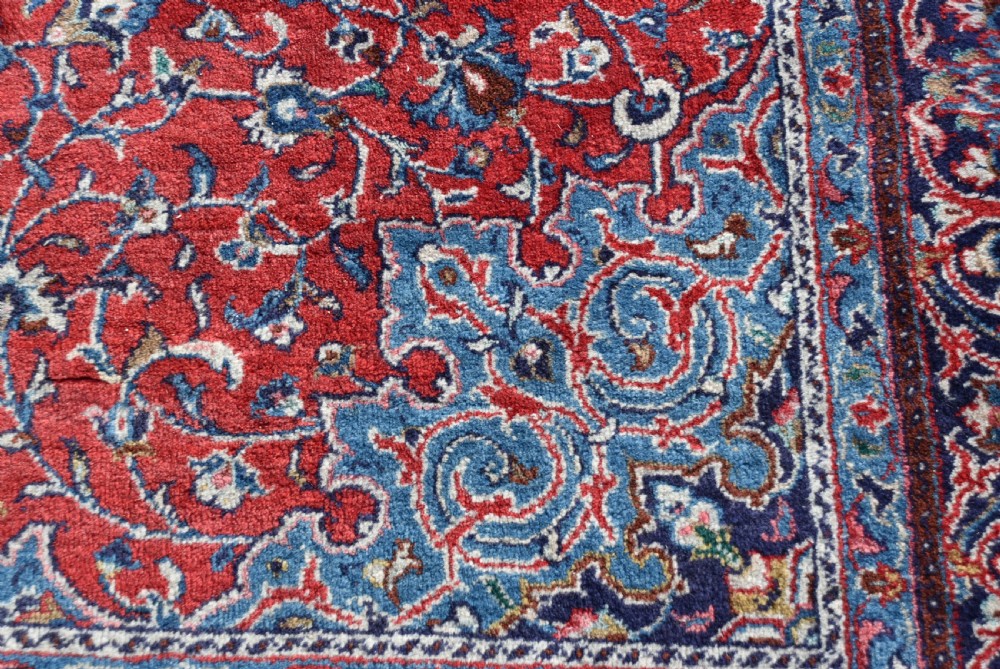A large hand-knotted vintage Persian rug featuring a central dark blue medallion surrounded by a detailed red field filled with floral arabesque patterns and framed by intricate borders. View X