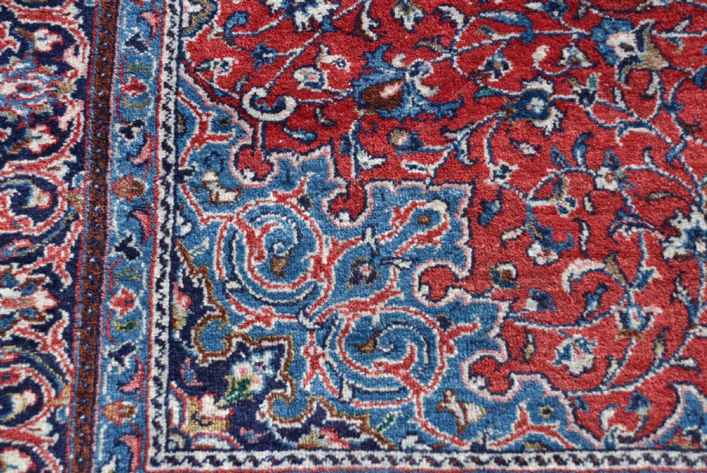 A large hand-knotted vintage Persian rug featuring a central dark blue medallion surrounded by a detailed red field filled with floral arabesque patterns and framed by intricate borders. View XI