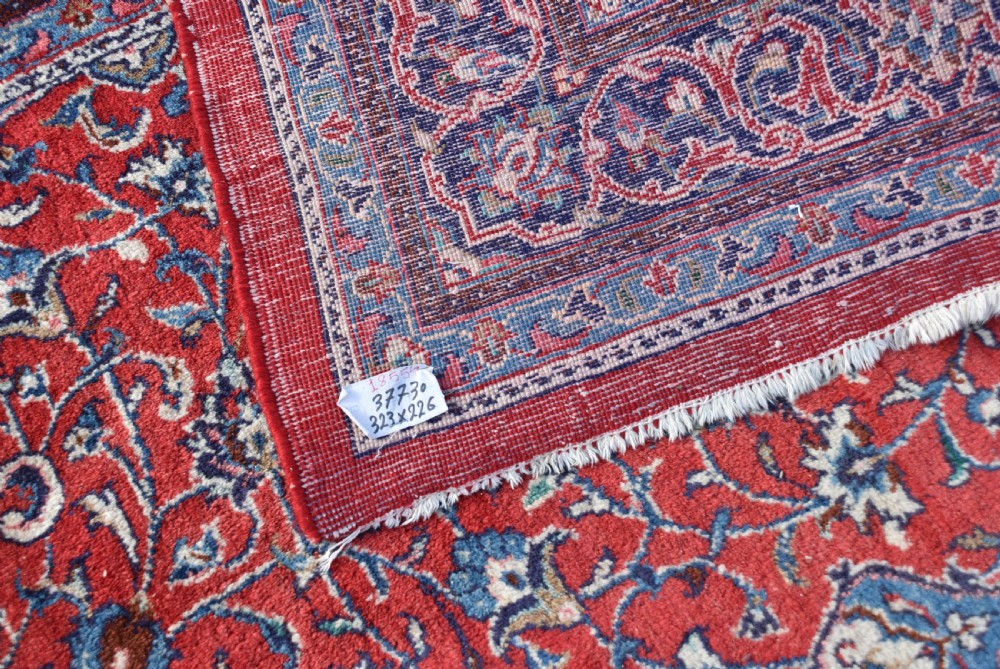 A large hand-knotted vintage Persian rug featuring a central dark blue medallion surrounded by a detailed red field filled with floral arabesque patterns and framed by intricate borders. View XII