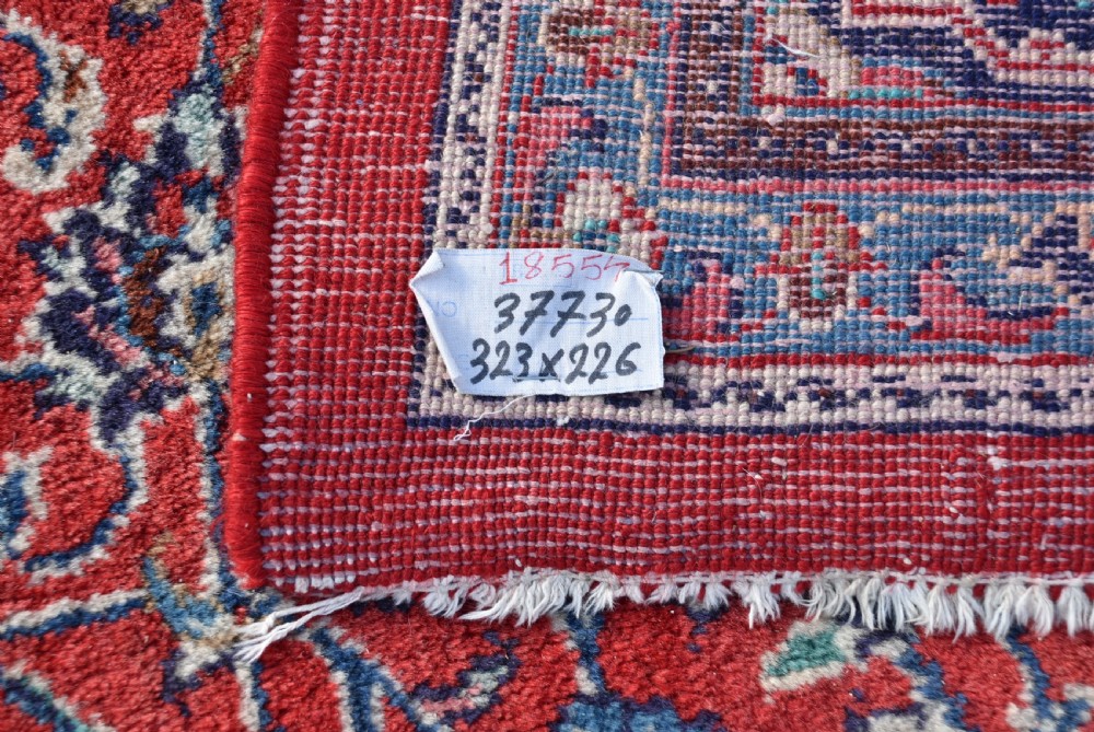 A large hand-knotted vintage Persian rug featuring a central dark blue medallion surrounded by a detailed red field filled with floral arabesque patterns and framed by intricate borders. View XIII