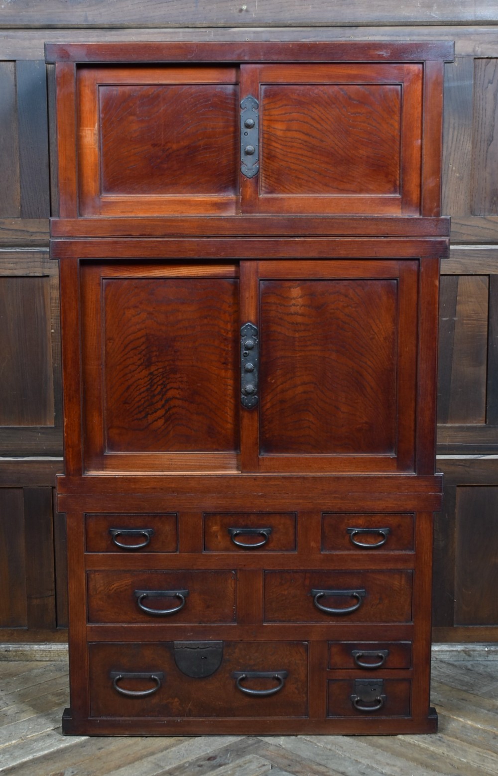 A stacked three-tier Japanese Tansu storage cabinet made of rich warm brown wood with iron handles and sliding panel doors.