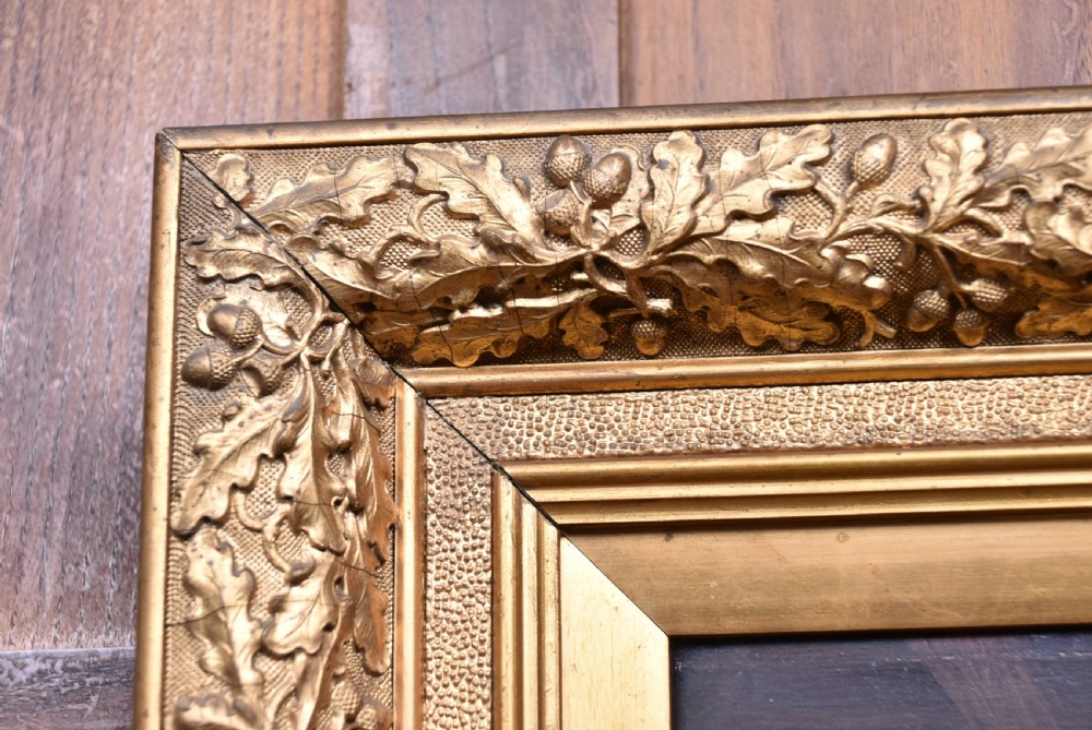 An oil painting depicting a woman working in a barn chopping vegetables beside a basket, housed within a gold carved frame decorated with oak leaves and acorns. View V