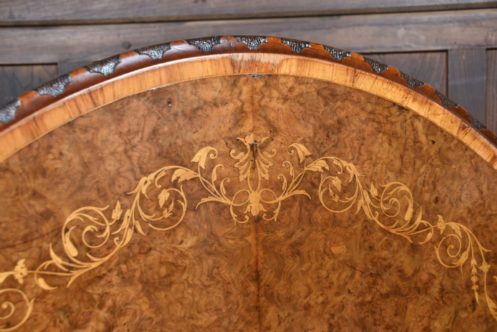 A Victorian oval burr walnut snap-top table featuring detailed floral marquetry inlay and a carved pedestal base displayed upright. View II