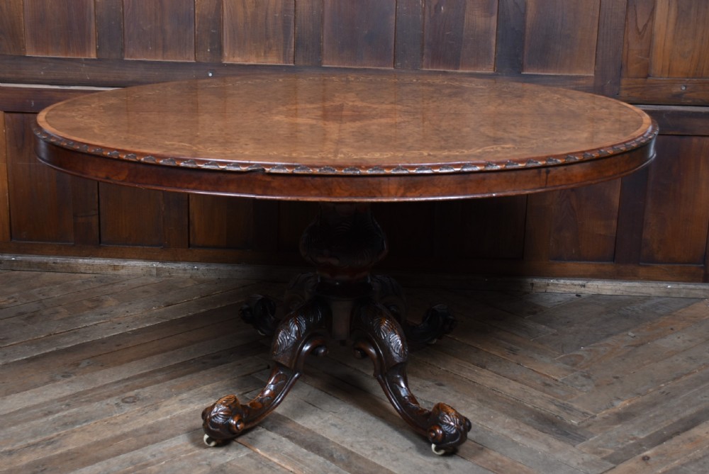 A Victorian oval burr walnut snap-top table featuring detailed floral marquetry inlay and a carved pedestal base displayed upright. View XI